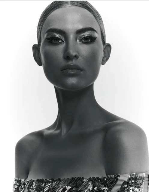 Striking black and white close-up of a woman with dramatic makeup and sequin top against a stark white background, capturing her intense gaze.