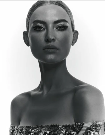 Striking black and white close-up of a woman with dramatic makeup and sequin top against a stark white background, capturing her intense gaze.