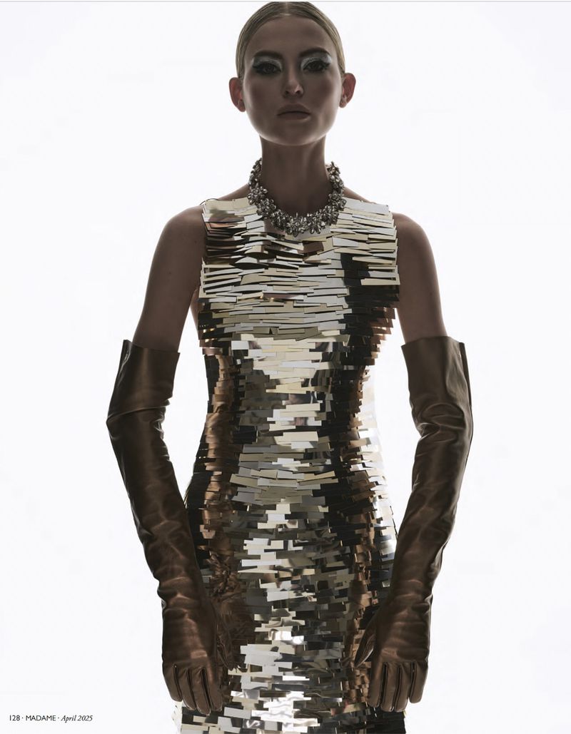 Glamorous fashion shot featuring a model in a silver sequin dress with long leather gloves and a statement necklace on a bright background.