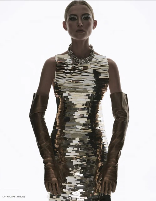 Glamorous fashion shot featuring a model in a silver sequin dress with long leather gloves and a statement necklace on a bright background.