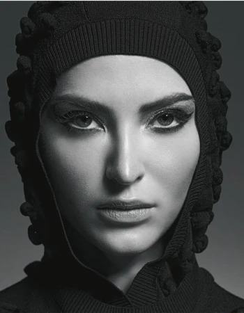 Close-up portrait of a woman wearing a black textured hooded garment against a dark studio gradient background.