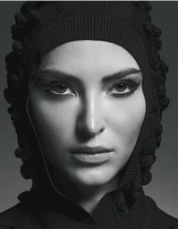 Close-up portrait of a woman wearing a black textured hooded garment against a dark studio gradient background.