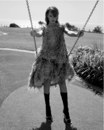 Model Daphne Maas standing on a swing wearing a textured dress and dark knee-high socks in an outdoor park setting