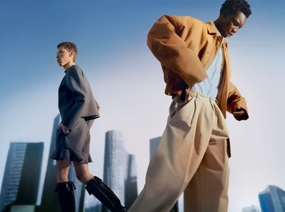 Two models posing against a skyline background, wearing stylish camel jacket and grey dress with boots.