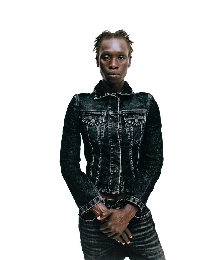 Close-up studio shot of a Black female fashion model wearing a distressed denim jacket and matching jeans, posing against a white backdrop.