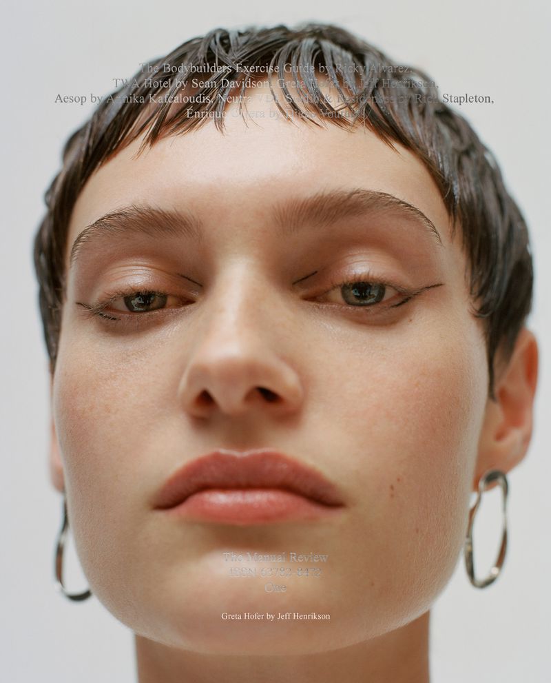 Close-up portrait of a woman with eyeliner and short brown hair, wearing silver earrings, against a white background, beauty-focused.