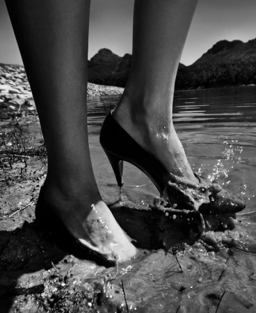 Close-up of legs standing in water with high heels splashing mud in black and white