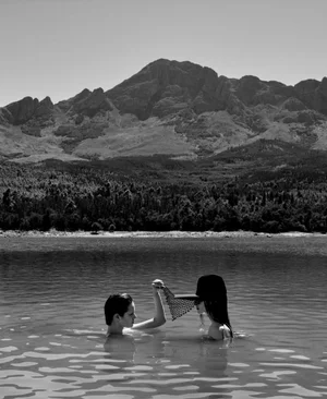Two models wading in a lake with a mountain range backdrop for M Le magazine du Monde
