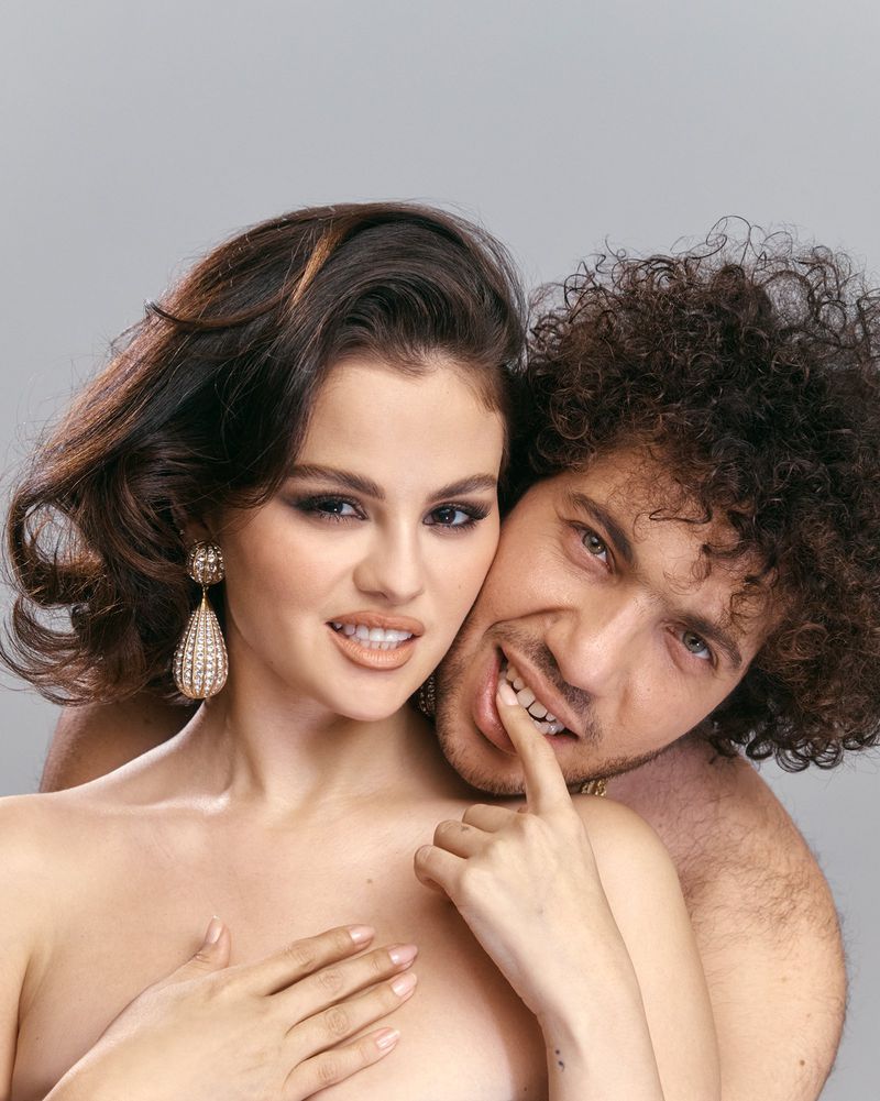 An intimate portrait captures a man and woman, embracing in a close-up studio shot with a neutral gray background, highlighting their connection.