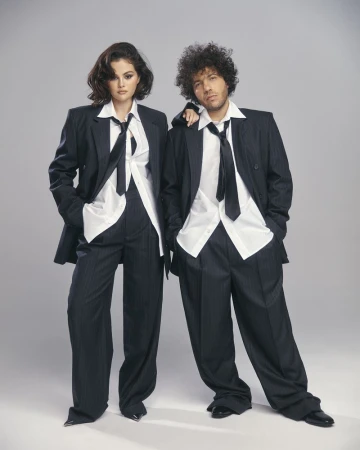 Two people wearing dark suits and light shirts stand in a photo studio, exuding a confident, stylish, and professional look.