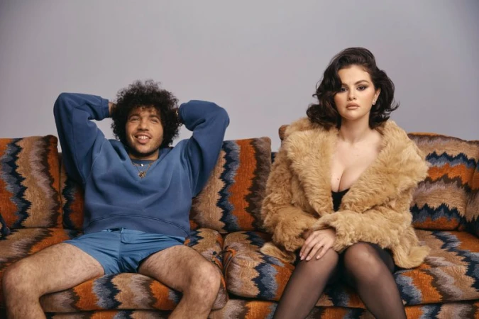 Benny Blanco and Selena Gomez seated on an orange patterned couch for an Interview Magazine editorial portrait by Roe Ethridge