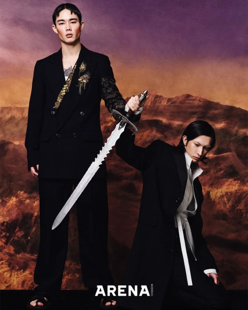 Two Asian men in suits pose with a decorative sword in a studio, against a backdrop of a mountain range for a fashion editorial.
