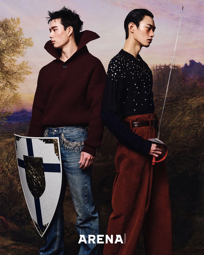 Two Asian men pose in an indoor photo studio setting with Renaissance-style background. One holds a shield, the other a sword.