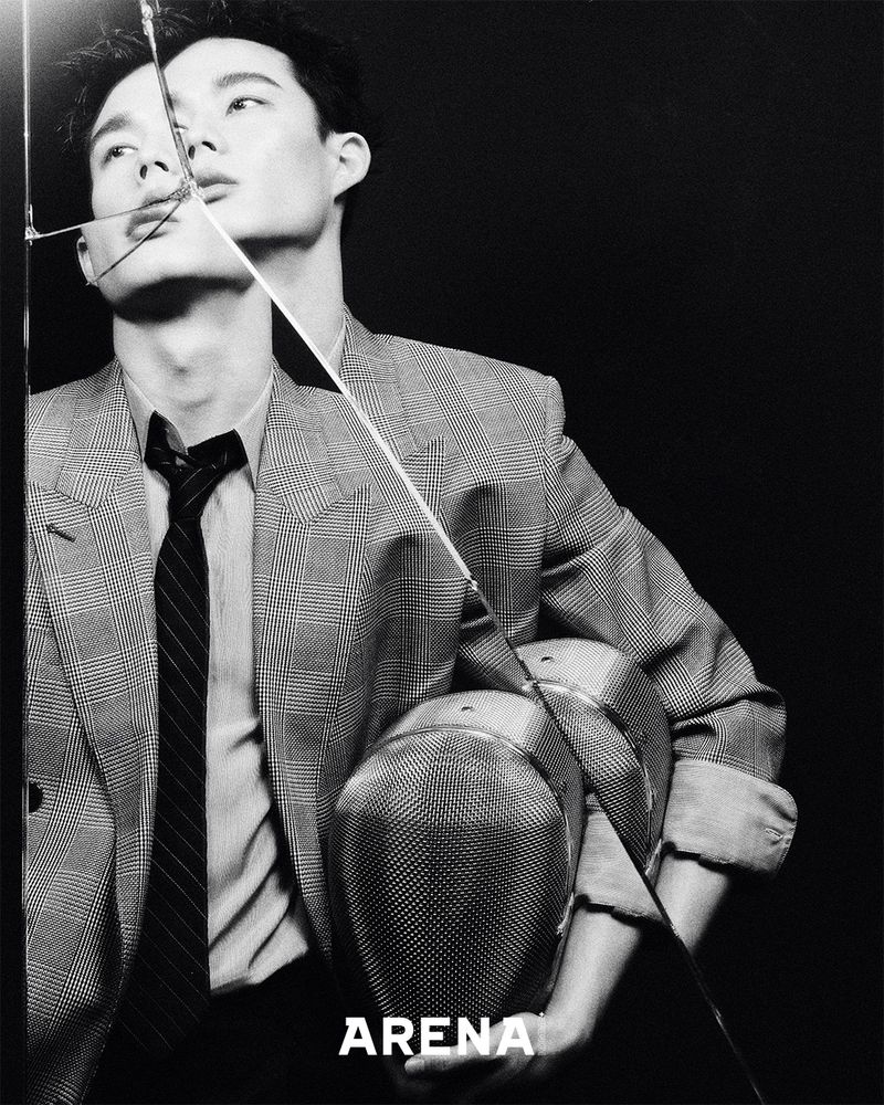 Black and white portrait of a stylish adult male wearing a blazer and tie, with a broken glass pane and 'ARENA' text overlay.