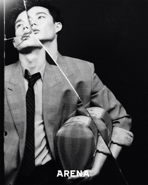 Black and white portrait of a stylish adult male wearing a blazer and tie, with a broken glass pane and 'ARENA' text overlay.