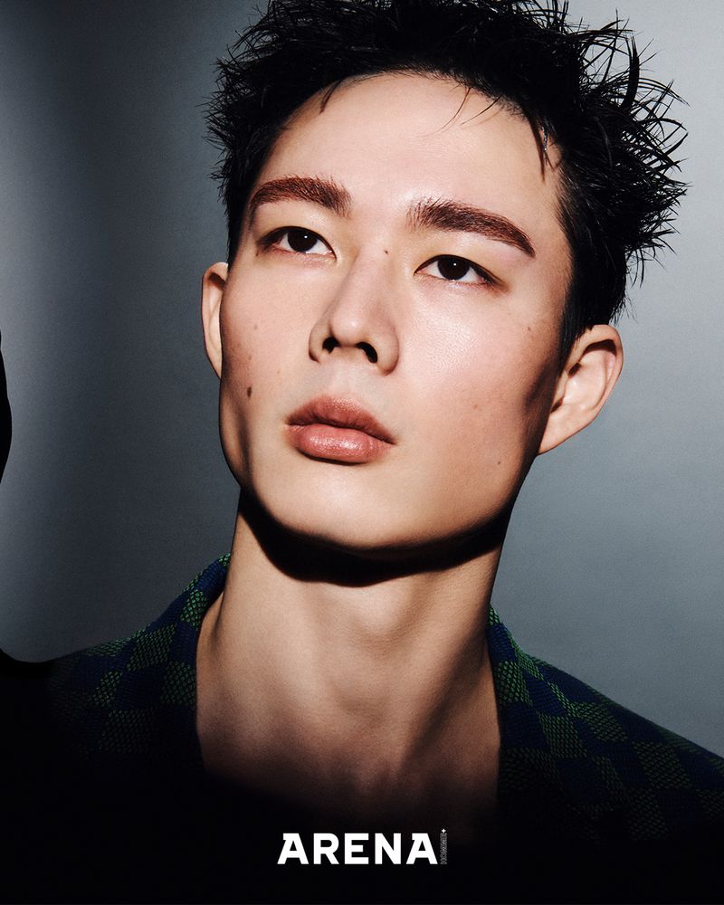 Portrait of a young adult male with a shadowed gray background, wearing a patterned shirt and featuring the 'Arena' logo.
