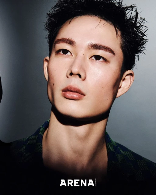 Portrait of a young adult male with a shadowed gray background, wearing a patterned shirt and featuring the 'Arena' logo.