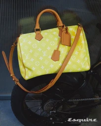 Bright yellow monogram leather duffle bag resting on the rear tire of a dark bicycle for an Esquire Korea editorial feature.