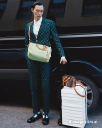 Asian male model wearing a green checker suit and handbag standing next to luggage in an Esquire Korea editorial