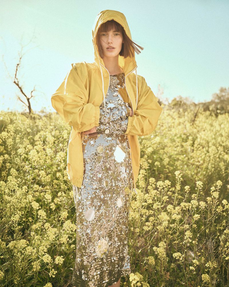 Woman in yellow raincoat and silver dress in a yellow flower field on a sunny day, fashion editorial photography.