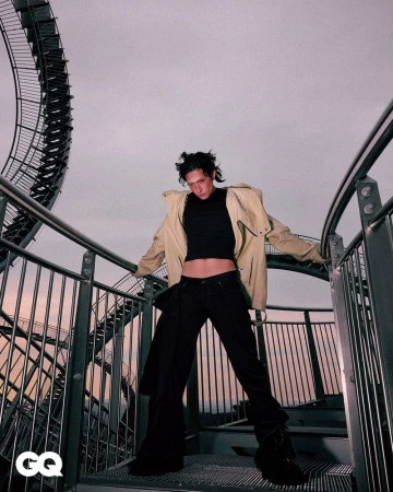 Adult posing on metal steps with industrial spiral structure backdrop. Fashion shot with modern clothes. Cloudy sky, overcast daylight.
