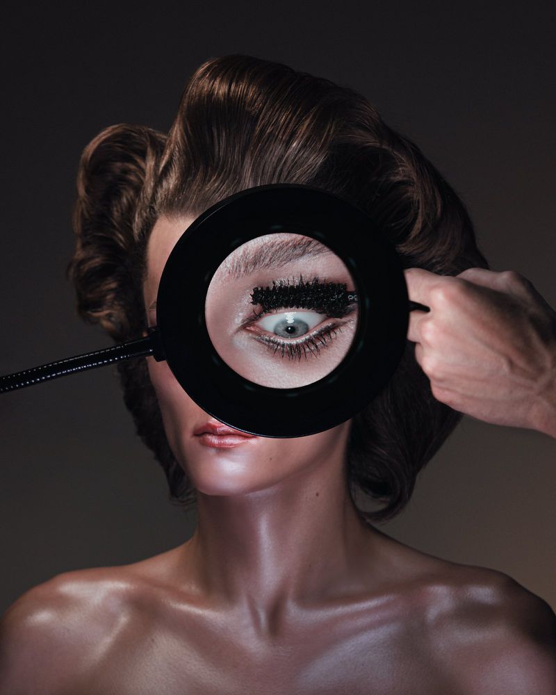 Close-up portrait of a woman getting makeup applied with a ring light highlighting her eye and long eyelashes.