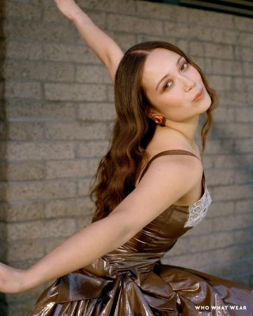 Laufey posing against a grey brick wall wearing a shiny bronze dress with lace trim, captured by Elena Rendina.