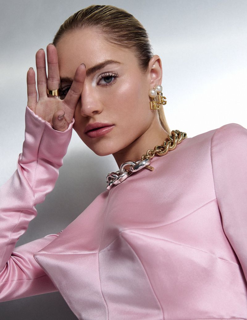 Michelle Randolph in a pink satin top with a gold chain necklace and pearl earrings, holding her hand near her face.