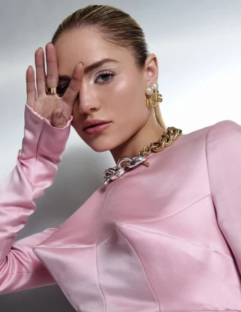 Michelle Randolph in a pink satin top with a gold chain necklace and pearl earrings, holding her hand near her face.
