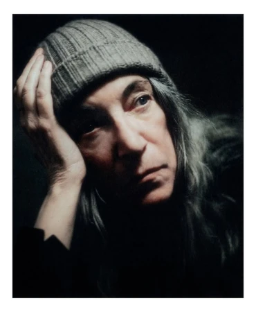 Portrait of Patti Smith wearing a ribbed knit beanie and dark clothing against a dark background, photographed by Boe Marion for Autre Magazine.