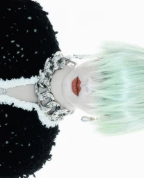 Close-up portrait of a model with green hair, pale face, bold red lips, and a chunky silver chain necklace against a white background.