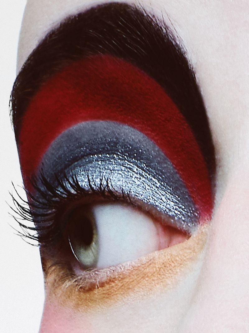 Macro close-up of eye makeup featuring vibrant red and silver eyeshadow, defined lashes, and a strong eyebrow.
