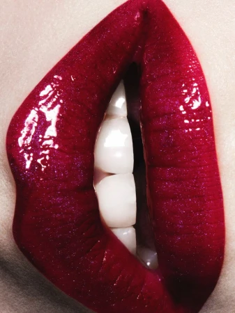 Close-up macro shot of glossy ruby red lipstick on lips with visible white teeth