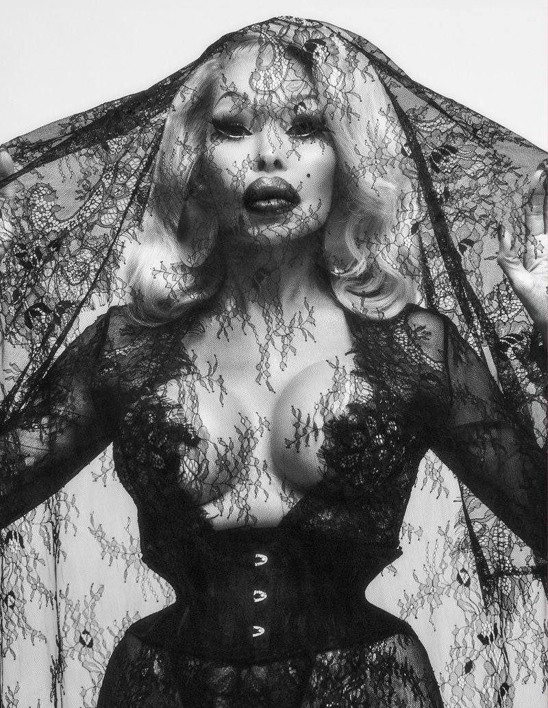 A captivating portrait of a person in a black lace outfit and veil against a bright background, highlighting textures and dramatic lighting.