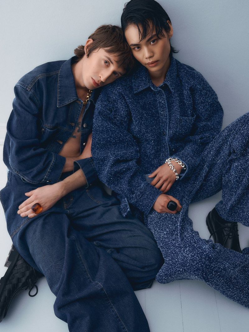 Two young adults pose indoors wearing matching denim jackets and pants in cool blue tones, complemented by visible jewelry.