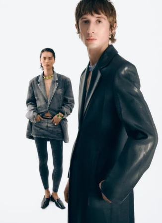Two models posing against a white background, wearing a black coat and a denim suit with dark leggings.
