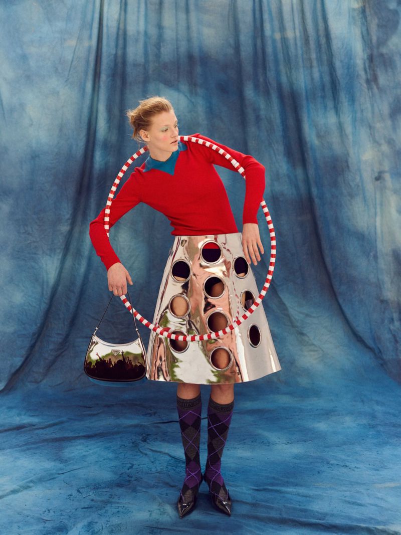 Fashion model poses with a red and white hula hoop wearing a shiny silver skirt with black and gray patterned socks in a studio.