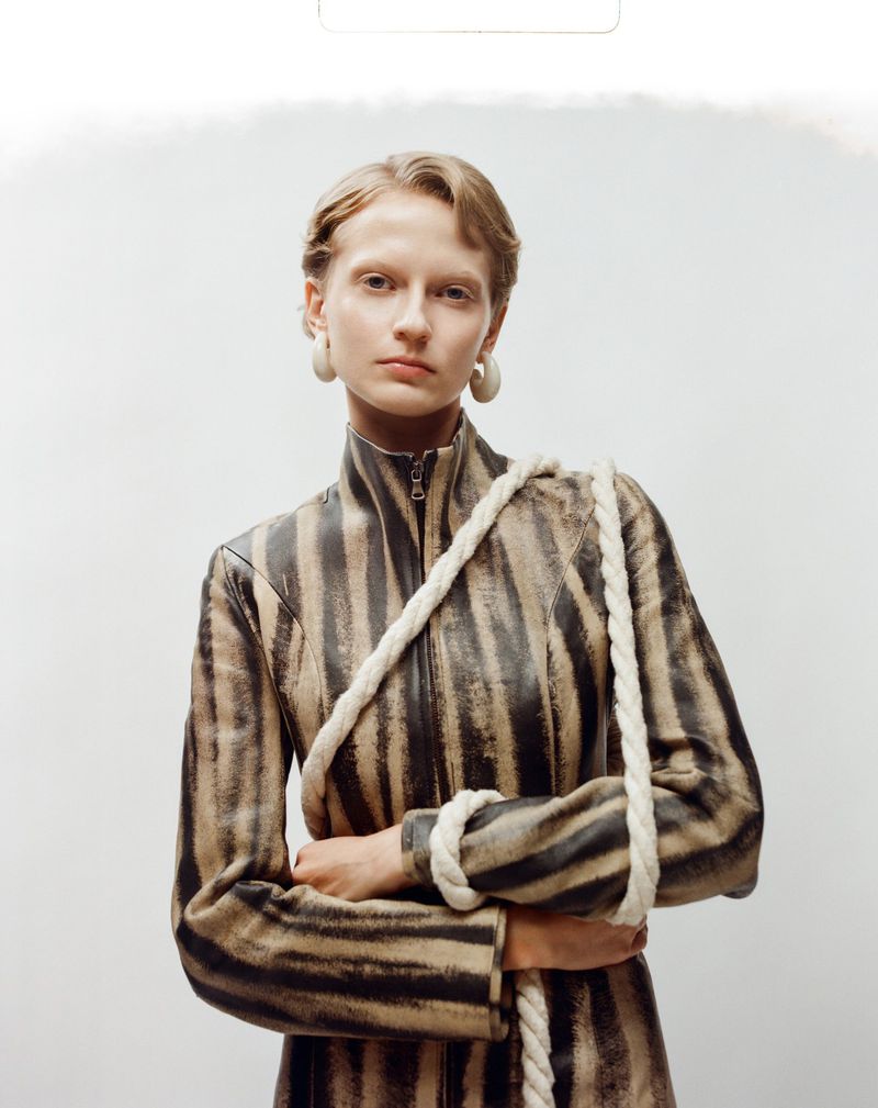Model with crossed arms wearing a striped jacket and thick white earrings against a white background