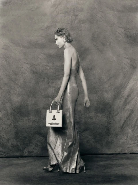 A woman in a shimmering gown holds a unique handbag in a studio setting, showcasing a blend of fashion and photographic art.