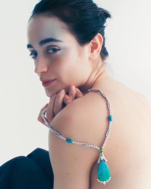 Close-up of an adult woman wearing a jeweled necklace with a blue and white gem pendant in a brightly lit indoor setting.