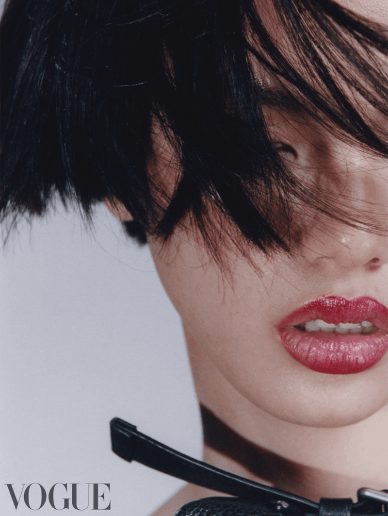 Close-up fashion portrait of a woman with short black hair and red lipstick wearing a black choker against a plain background.