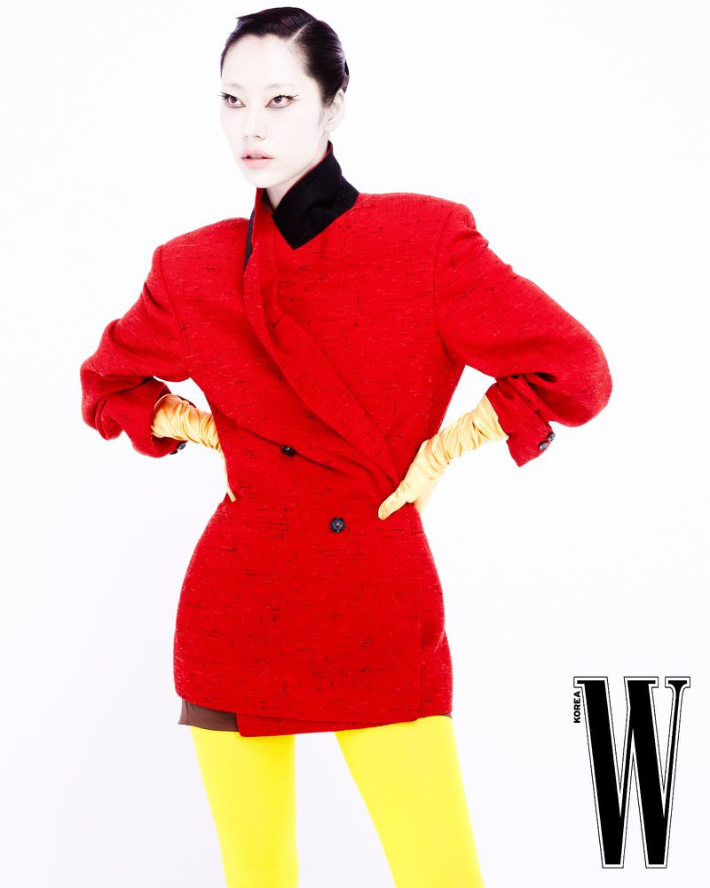Fashion shot of a slender adult woman in a red double-breasted blazer, yellow leggings, and yellow gloves against a white background.