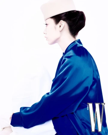 Profile view of a model in a vibrant blue satin jacket and pillbox hat against a white background for W Korea