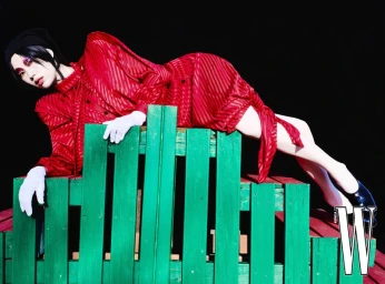 Model in a red dress and white gloves lying across a green wooden structure against a black background for W Korea.
