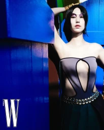 Model with dark hair and glittering eye makeup leaning against a bright blue wall wearing a strapless cutout dress