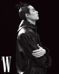 Black and white portrait of a male model in profile with arms crossed wearing a dark jacket against a dark background