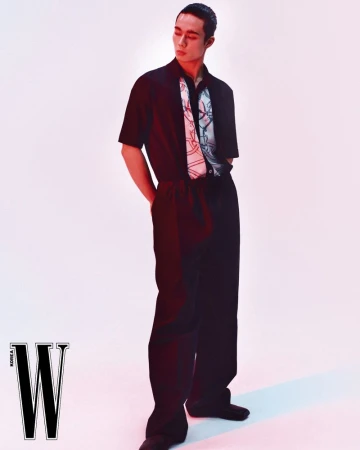 Model wearing a black short-sleeve shirt with a patterned scarf detail and dark trousers against a white backdrop.