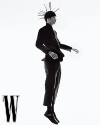 Model in black jacket and trousers wearing spiky headpiece against bright white background