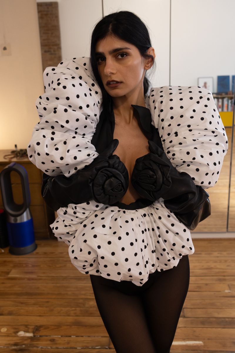 Woman wearing a puffy polka dot top with black leather accents poses indoors with natural light, creating a unique fashion portrait.