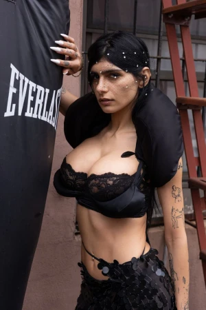 Brunette woman in a black bra poses beside an Everlast punching bag in front of a brick building with fire escape.